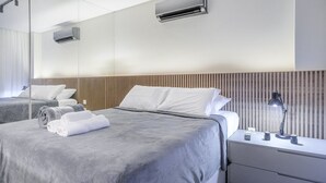 A modern hotel room with a large bed, a bedside table with a lamp, and a wall-mounted air conditioner. - Cozy Studio Near the sea in Salvador Mpa107 (Salvador)
