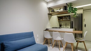 A modern kitchen with a built-in microwave, a refrigerator, and a gas stove. There is a blue sofa and four white chairs in the living area. - Cozy Studio Near the sea in Salvador Mpa107 (Salvador)