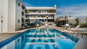 A swimming pool with tiled flooring, surrounded by lounge chairs and potted plants. - Cozy Studio Near the sea in Salvador Mpa107 (Salvador)