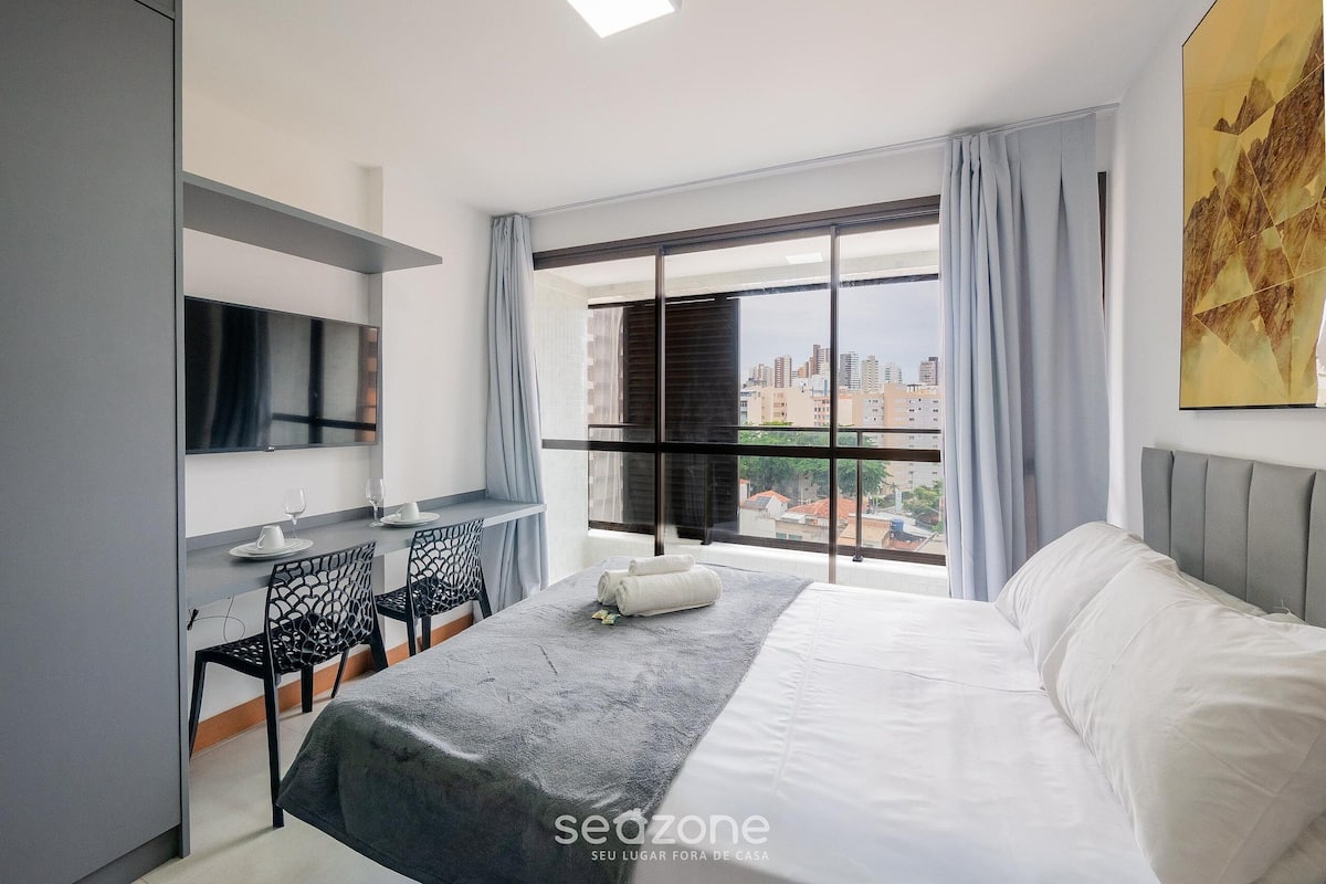 Camera d'albergo moderna con un letto, una scrivania e un'ampia finestra con vista sulla città.