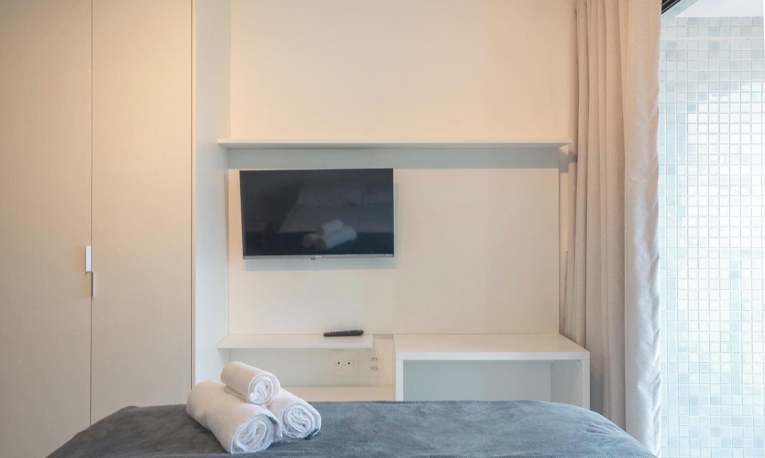 Una camera d'albergo con un letto, una TV a muro, un tavolino e una finestra con tende.