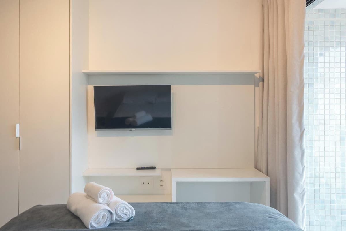 Una camera d'albergo con un letto, una TV a muro, un tavolino e una finestra con tende.