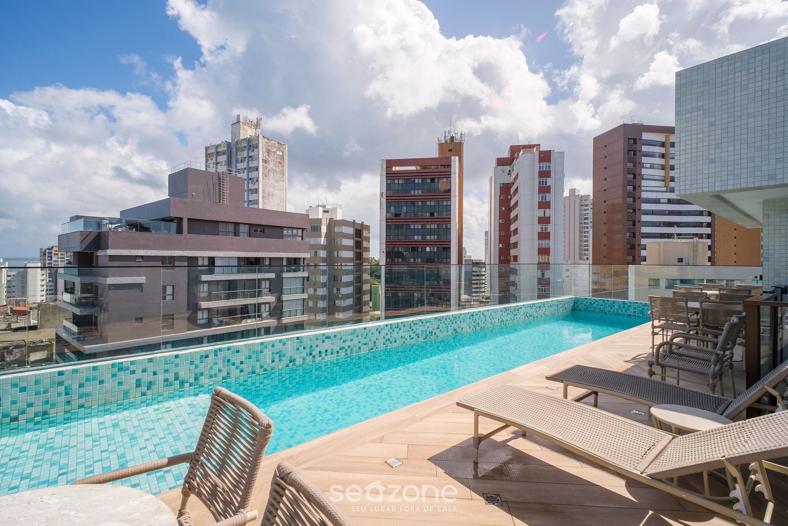 Ein Pool auf dem Dach mit Liegestühlen, ein mit Fliesen ausgelegter Pool und moderne Gebäude im Hintergrund.