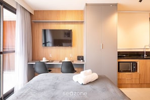 A modern hotel room with a bed, a desk, a TV, a microwave, and a window with curtains. - Modern and Fully Equipped Apartments 500m From Barra Beach in Salvador ZBN (Salvador)
