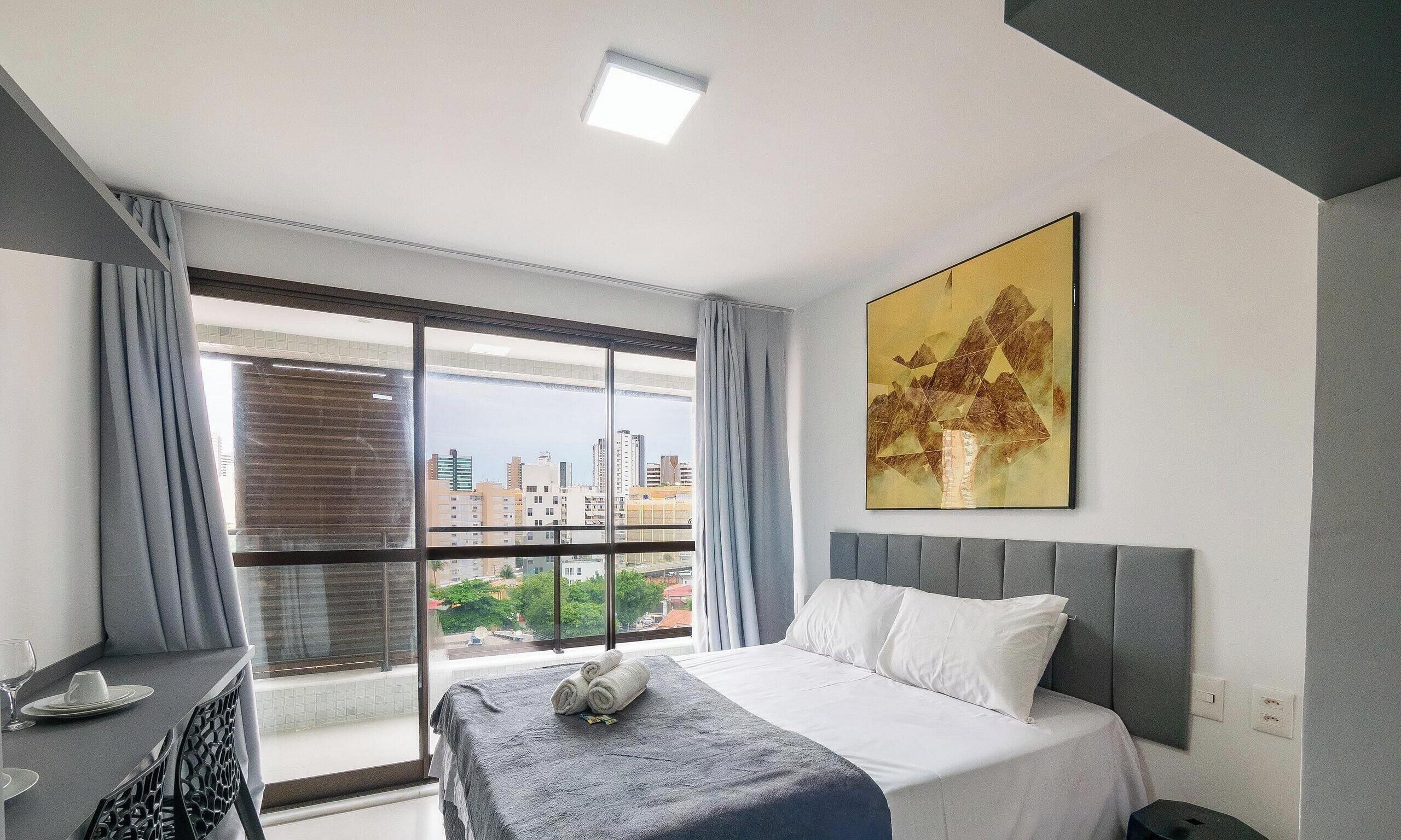 A hotel room with a bed, a desk, a chair, a window with curtains, and a city view.