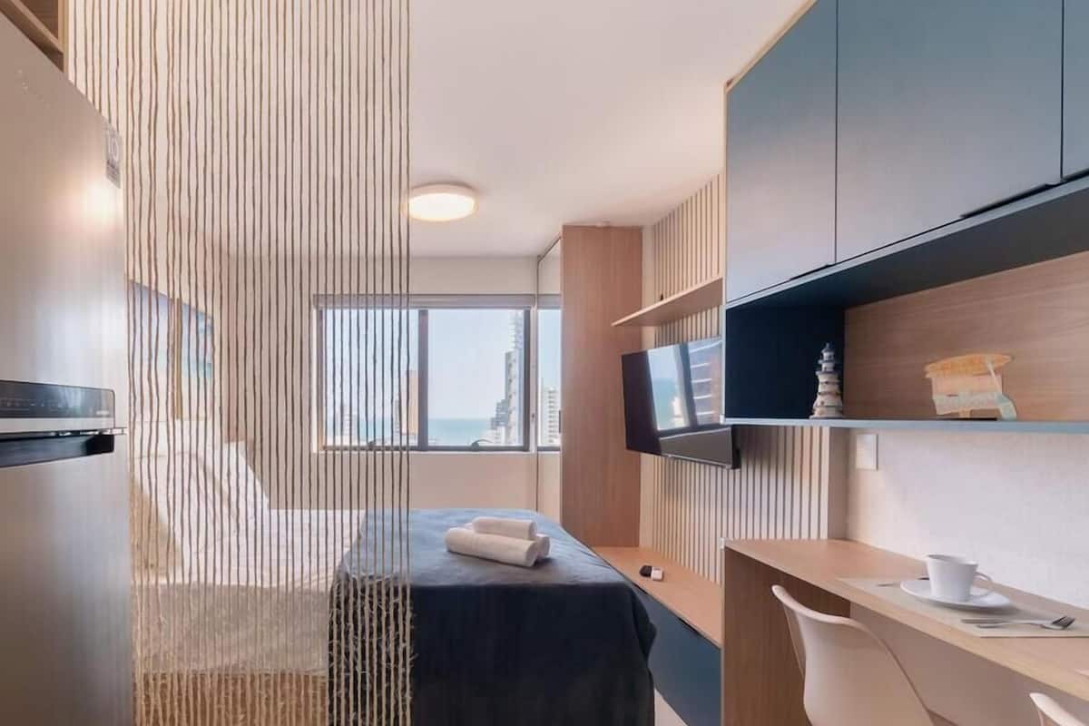 Una camera d'albergo moderna con un letto, una scrivania, una televisione e vista sulla città.