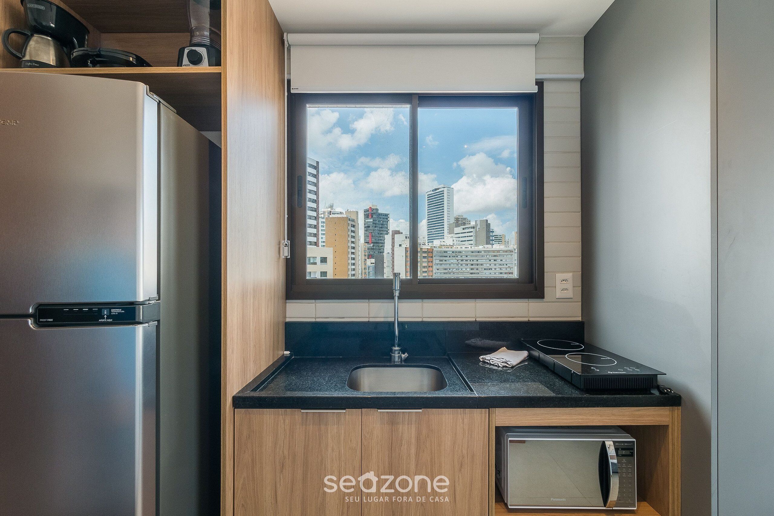 A modern kitchen with a stainless steel refrigerator, a built-in microwave, a sink, and a window with a city view.