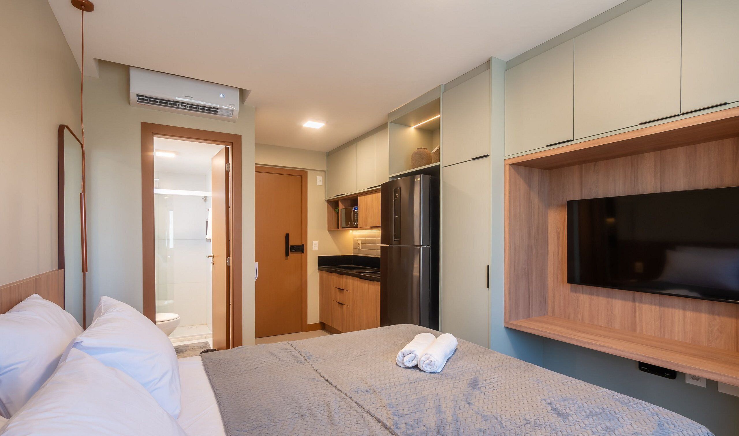 Una camera d'albergo con un letto, una TV a muro, un angolo cottura e un bagno.