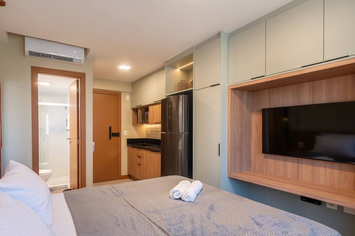 Una camera d'albergo con un letto, una TV a muro, un angolo cottura e un bagno.