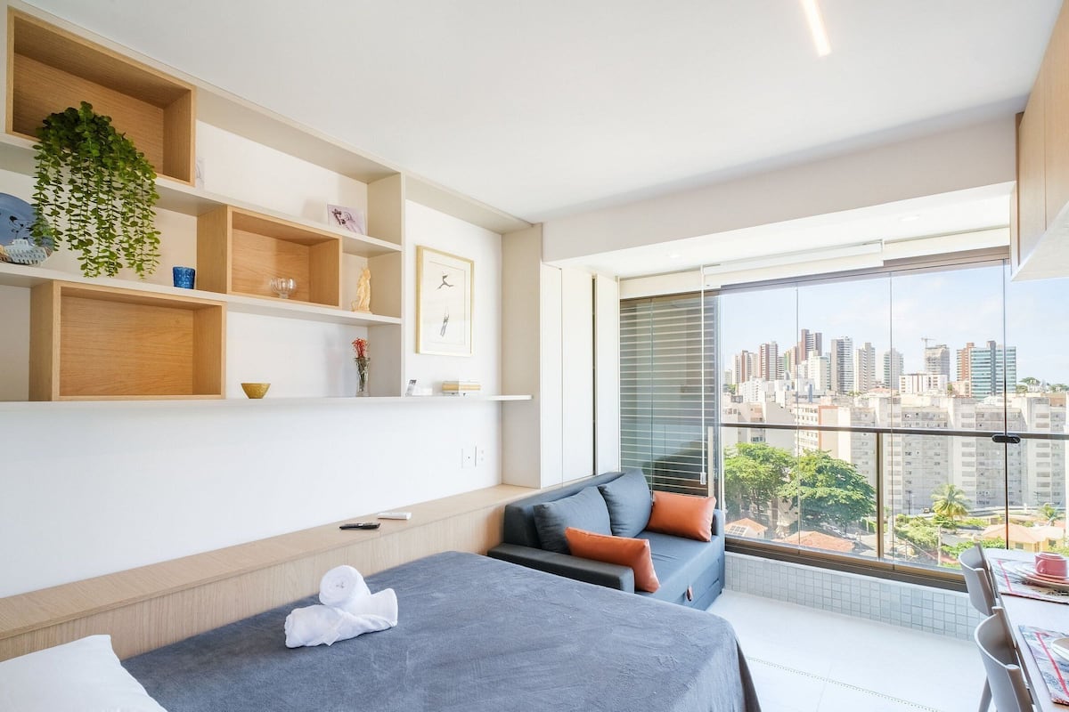 Una camera d'albergo moderna con un balcone, un divano, un letto e una mensola a parete con oggetti decorativi.