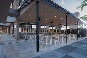 An outdoor seating area with tables and chairs, a covered roof, and a building entrance. - Raia Beach Resort Port Dickson (Port Dickson)
