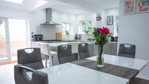 A modern kitchen with a central island, white cabinetry, and a dining area with grey upholstered chairs. - Hillview Modern 3 Bed Bromley, Chislehurst House (Greater London)