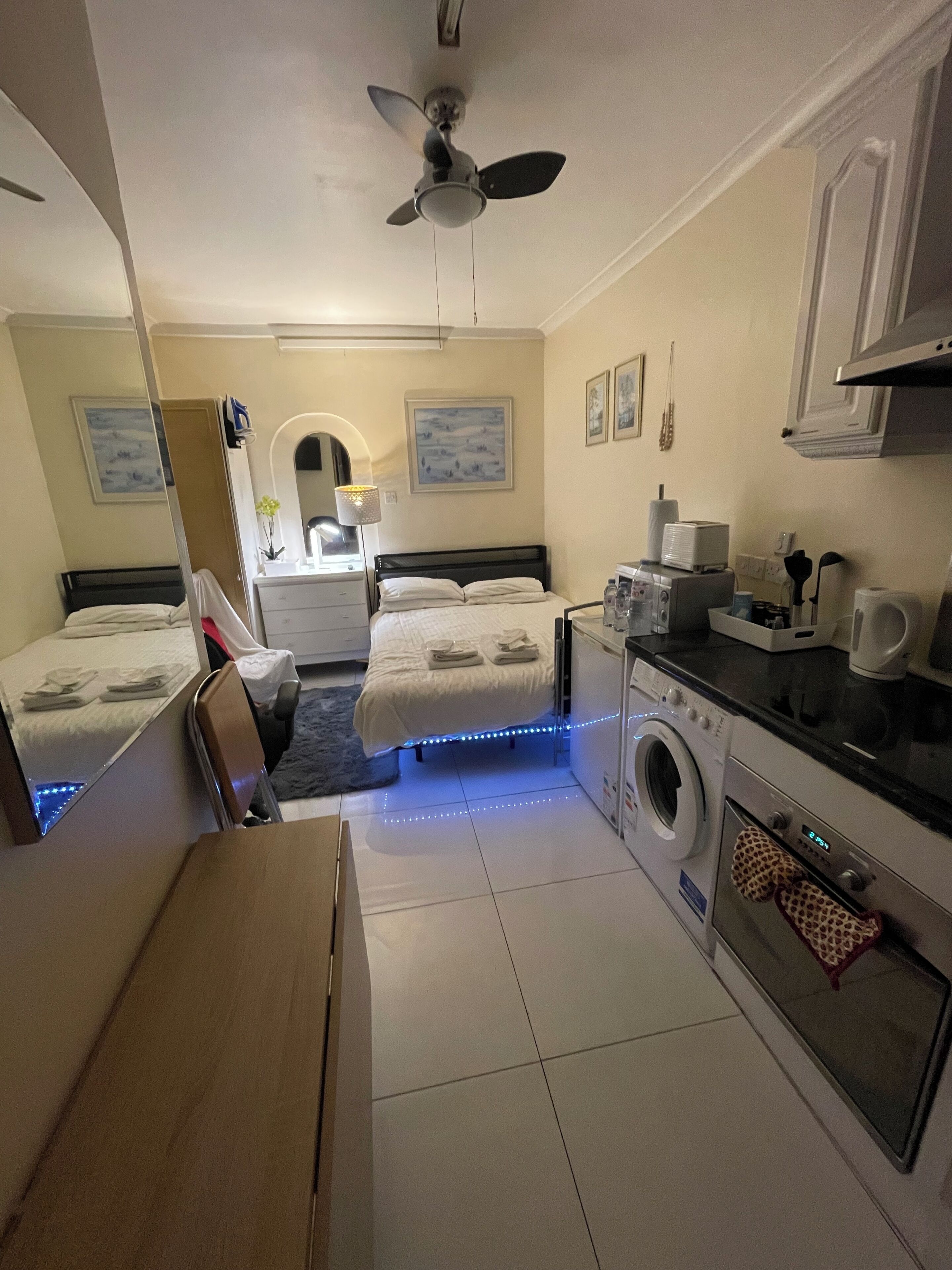 A compact hotel room with two beds, a washing machine, a kitchenette, and a ceiling fan.