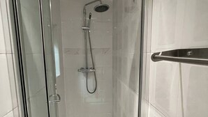 Une douche moderne dotée d’une porte en verre, d’un pommeau de douche à main et d’un robinet mural.
