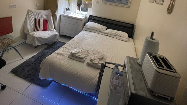 Une chambre d’hôtel avec un lit, une table de chevet, une lampe et un ventilateur de plafond.