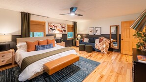 Un dormitorio moderno con una cama grande, una mesita de noche, un banco, un sofá, un ventilador de techo y una puerta de madera.