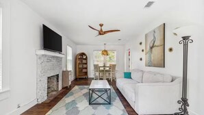 A living room with a white sofa, a coffee table, a fireplace, a TV, and a ceiling fan.
