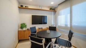A conference room with a round table, four chairs, a flat-screen TV, and a shelf above the TV. -  Apartamentos em Prédio c/Academia na Ondina-SSA-HOA (Salvador)