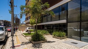 Un edificio moderno con grandes ventanales, un sendero adoquinado con pavimentos táctiles y macetas con plantas verdes.