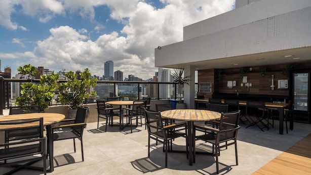 Una terraza en la azotea con mesas al aire libre, zona de bar y vistas a un horizonte urbano.