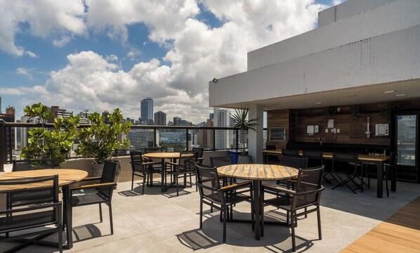 A rooftop terrace with outdoor seating, a bar area, and a city skyline view.
