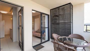 A modern interior with a glass door leading to a bedroom, wicker furniture, and a black slatted partition.
