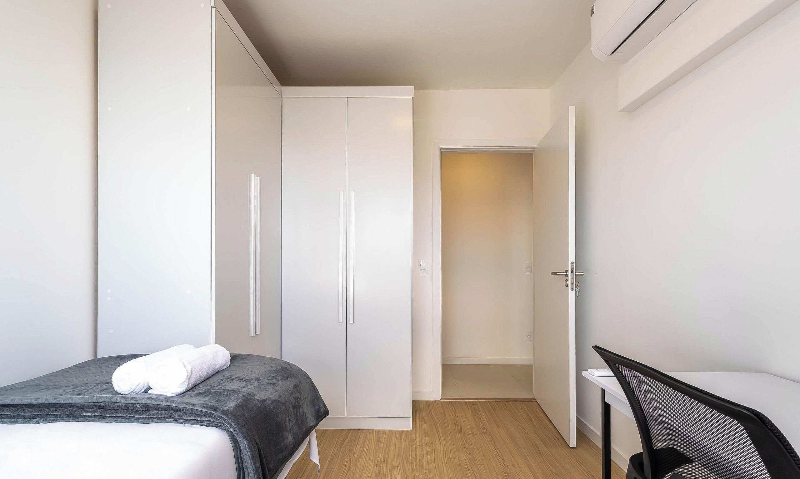 A bedroom with a bed, a desk, and a wardrobe.