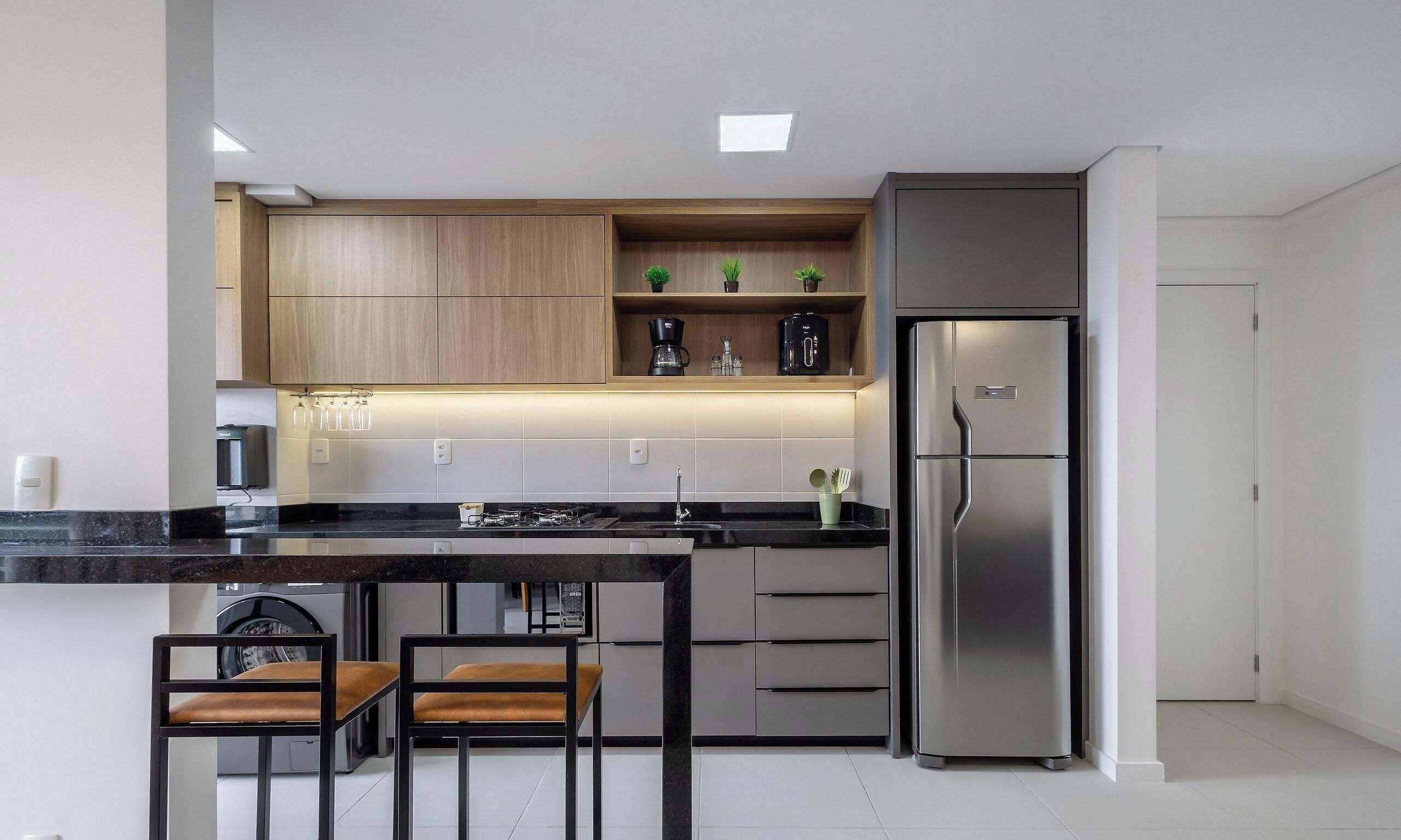 A modern kitchen with a stainless steel refrigerator, wooden cabinets, and a black countertop.