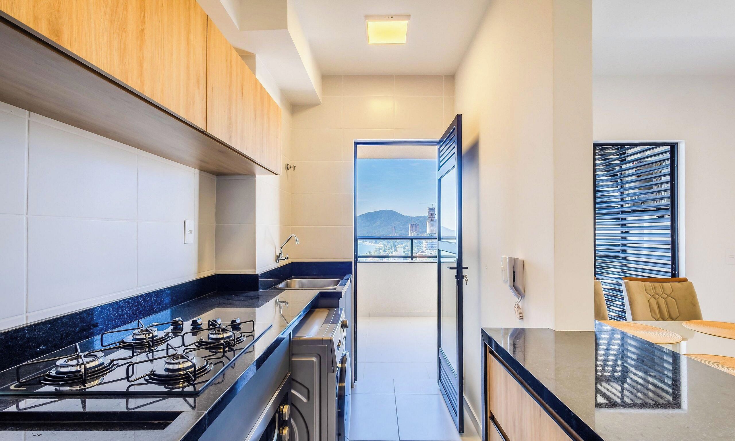A modern kitchen with a gas stove, a sink, and a view of a cityscape through an open door.