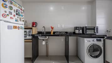 A modern kitchen with a refrigerator, microwave, washing machine, and a sink with a faucet.