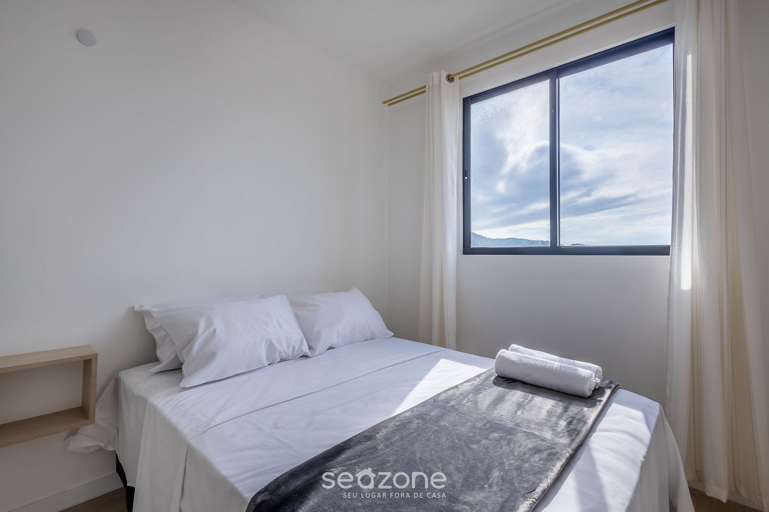 A bedroom with a bed, a window, and a view of the sky.