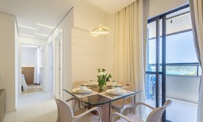 Een moderne eetruimte met een glazen tafel, witte stoelen en een uitzicht op het groen door grote ramen.