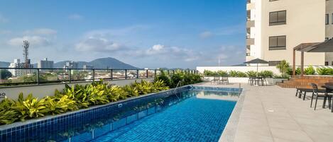 Una piscina en la azotea con suelo de baldosas, rodeada de vegetación y mobiliario de exterior.