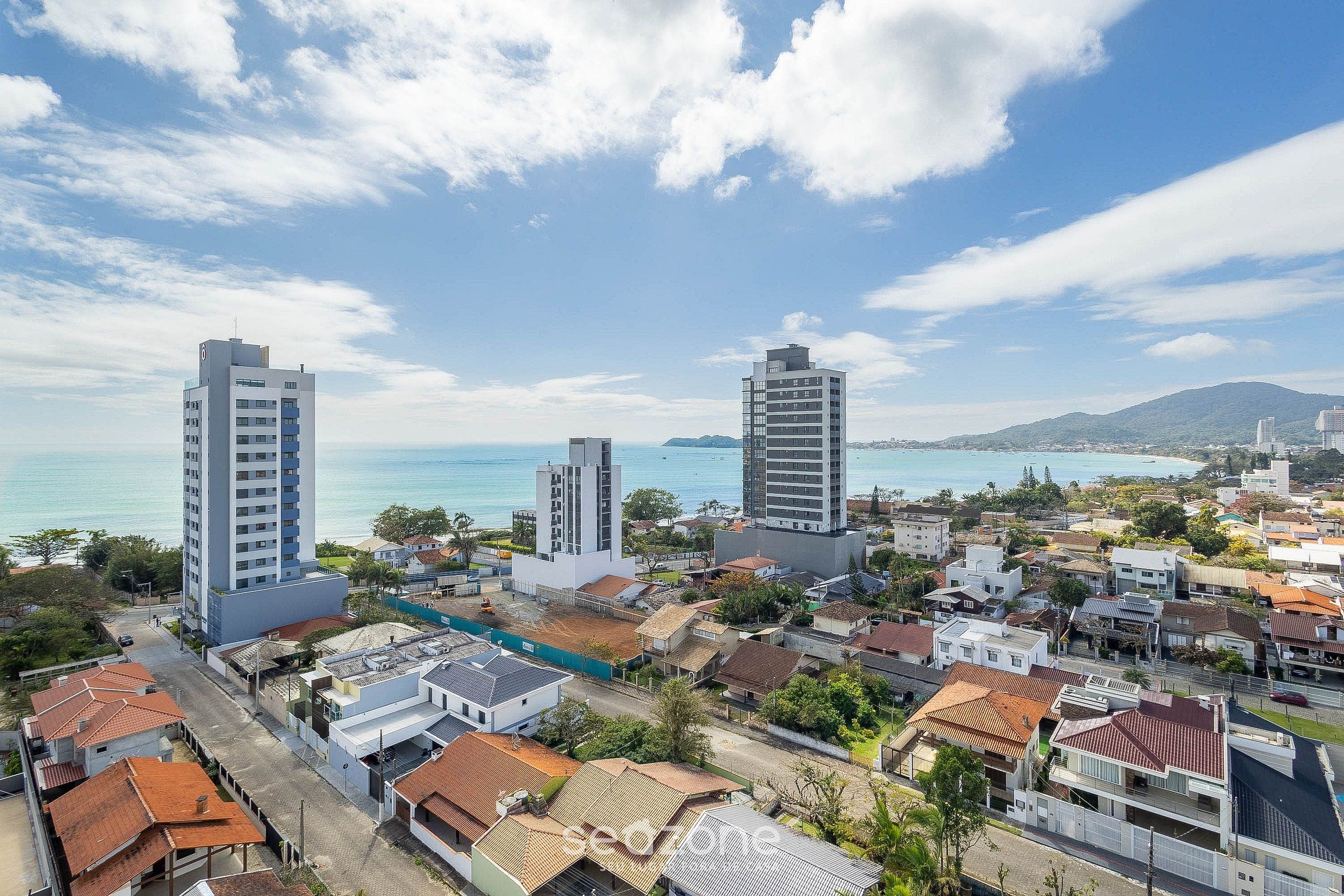 A coastal cityscape with modern buildings, a clear sky, and a view of the sea.