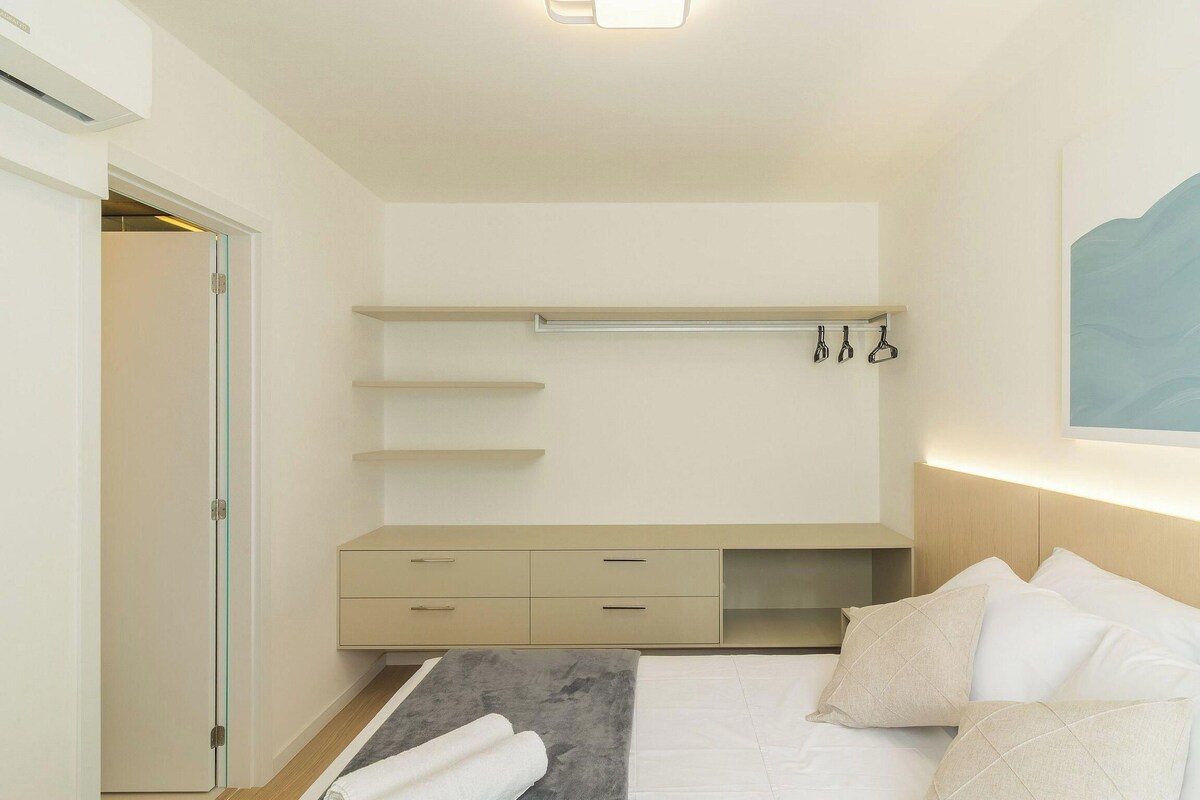 Une chambre à coucher au style minimaliste, avec un lit, des tables de chevet et une étagère fixée au mur.