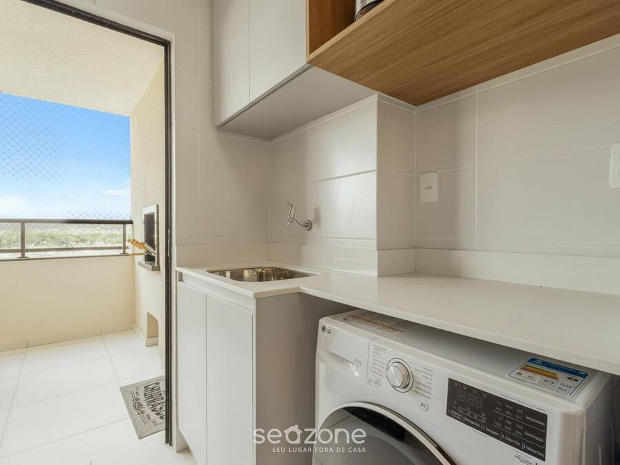A laundry room with a washing machine, a sink, and a wooden shelf.