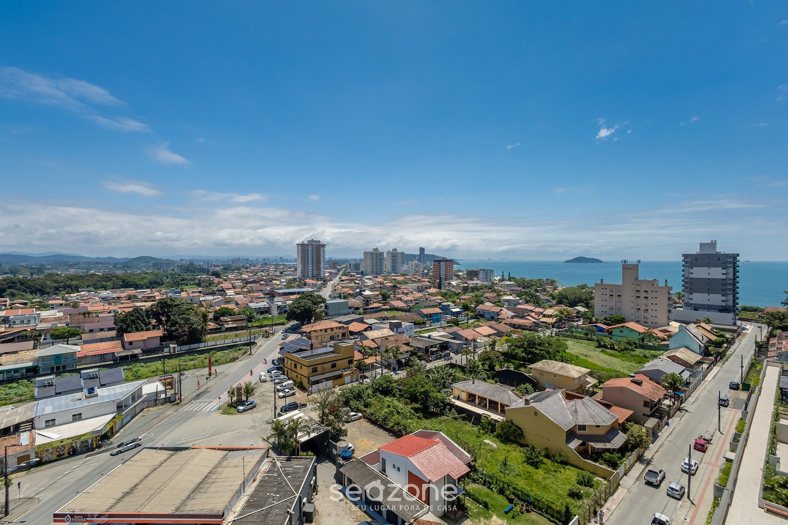 A coastal cityscape with residential buildings, a prominent high-rise, and a clear view of the sea.