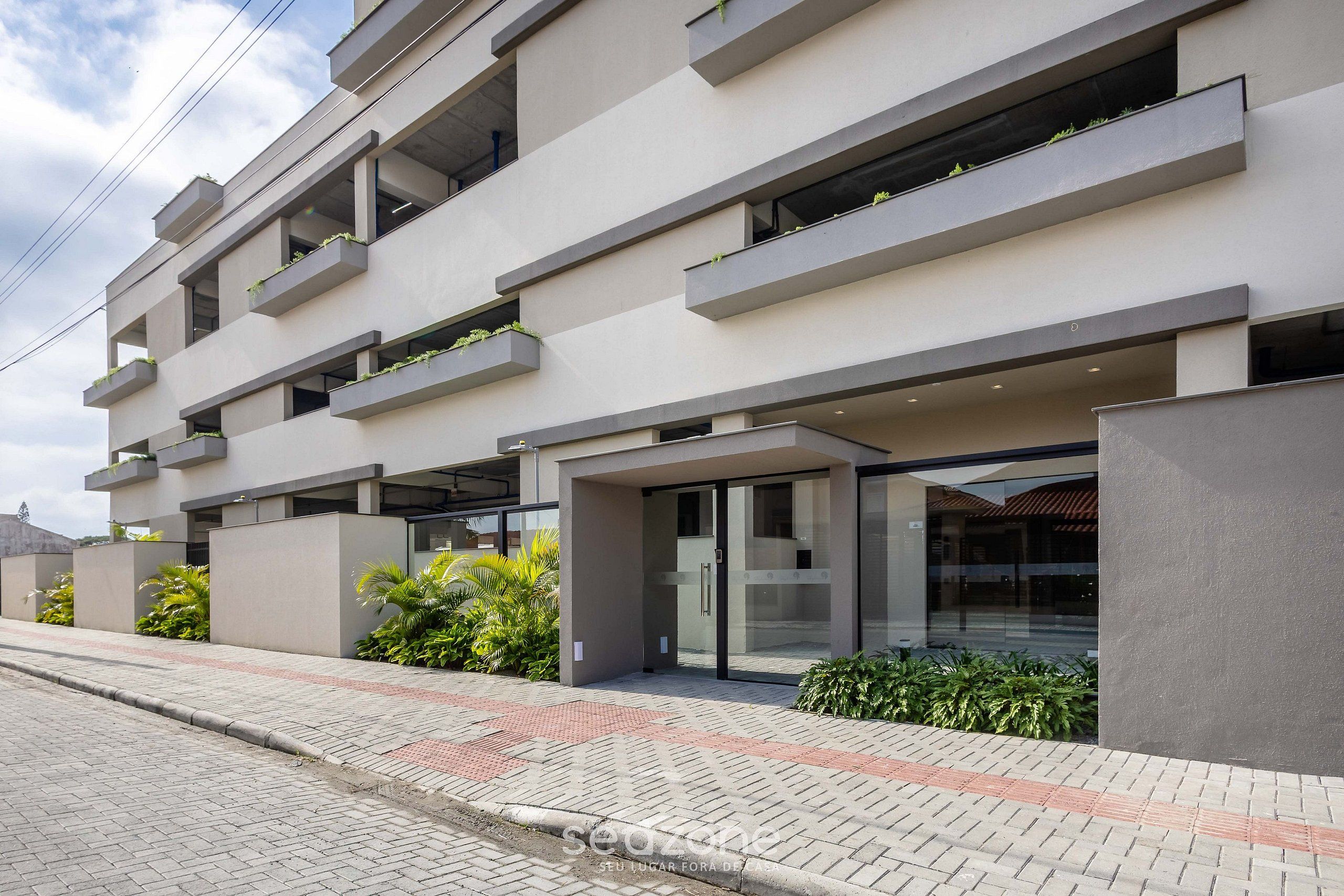 Un edificio moderno con varios balcones, entrada de vidrio y un camino pavimentado.