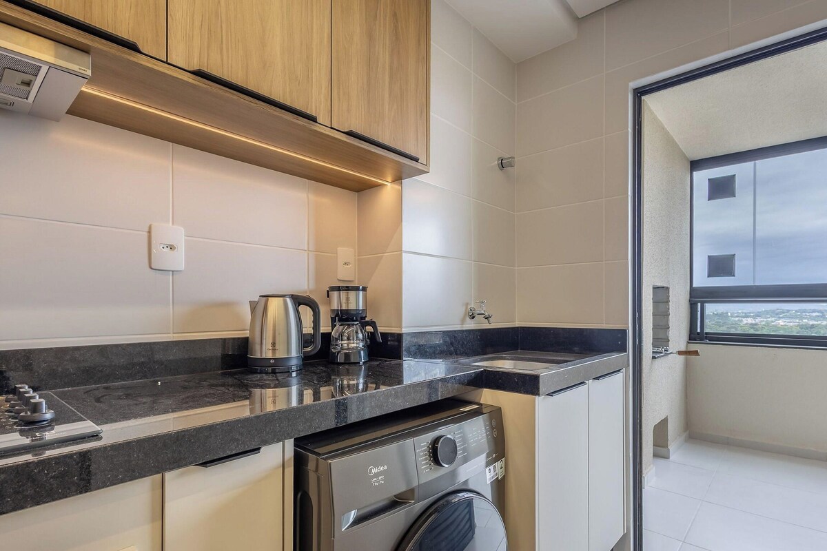 A compact kitchen with a built-in oven, a coffee maker, and a kettle on the counter.
