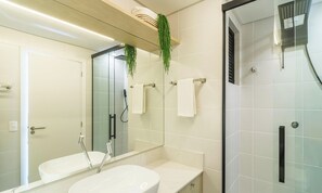 Een moderne badkamer met een douchecabine van glas, een witte wastafel en een spiegel.