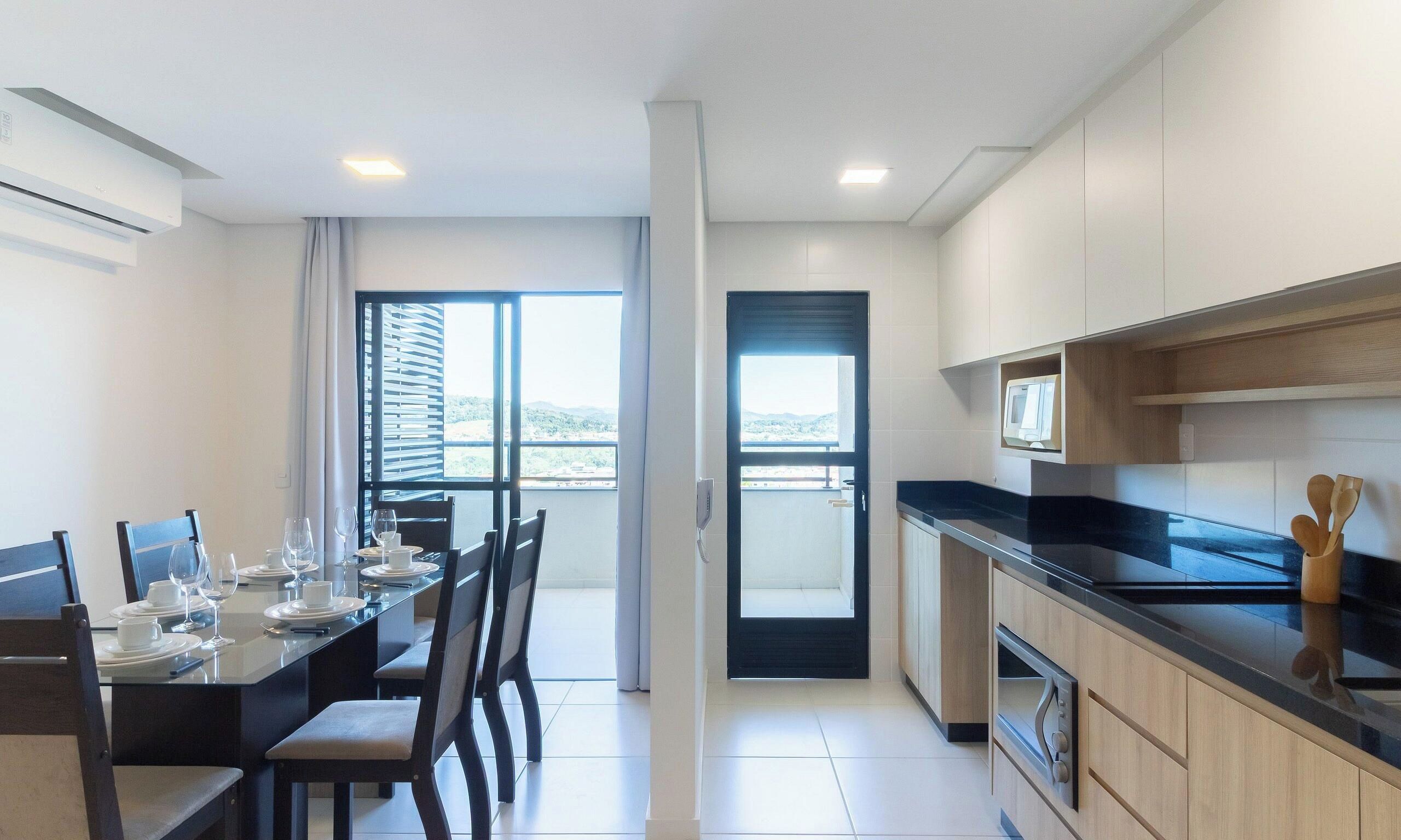 A modern kitchen with a dining area, a black countertop, and a view through the door.
