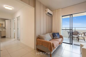 A modern living room with a sofa, a balcony with wicker furniture, and an air conditioning unit.
