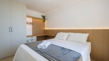 A hotel room with a bed, a bedside table, a wardrobe, and a small shelf with a plant.