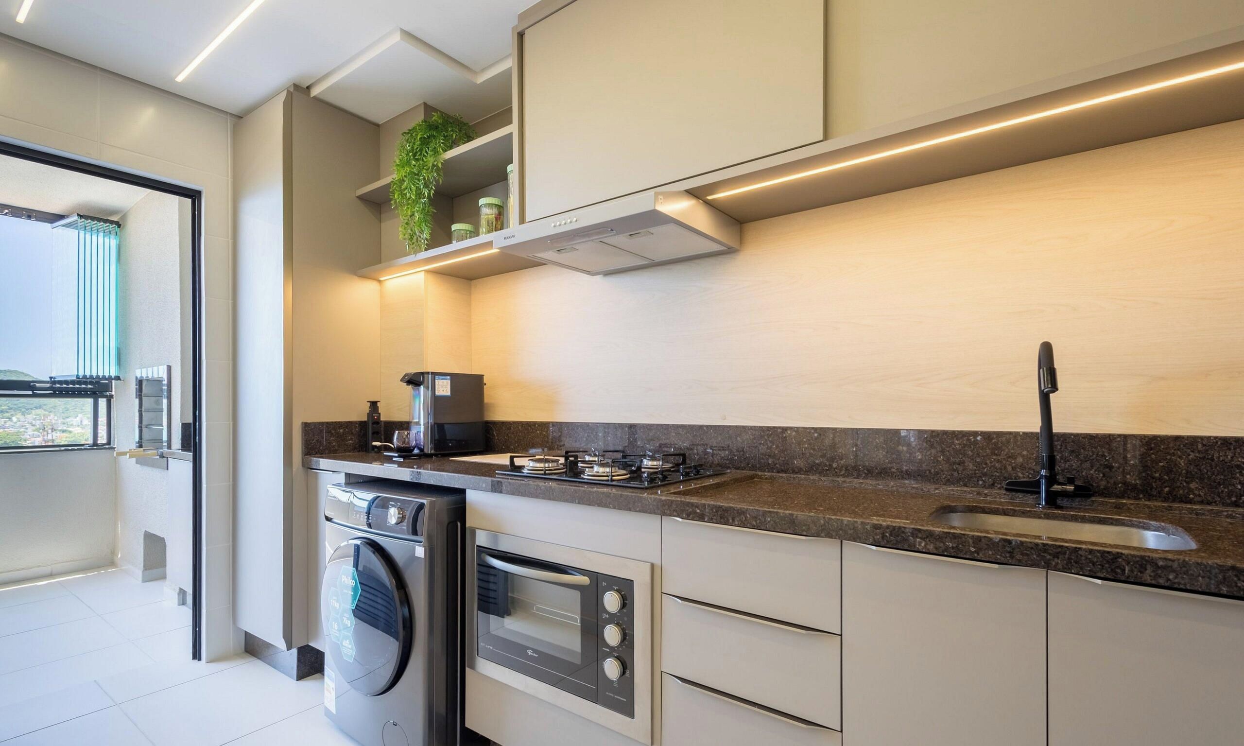 Et moderne køkken med indbyggede hårde hvidevarer, en stålvask og et vindue med udsigt til en balkon.