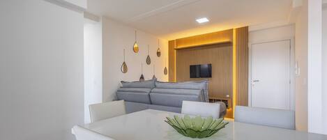 A modern dining area with a white table, grey sofa, and a decorative plant.