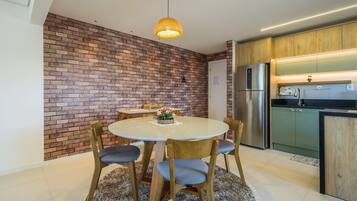A modern kitchen with a brick wall, a dining area with a round table and chairs, and a refrigerator.