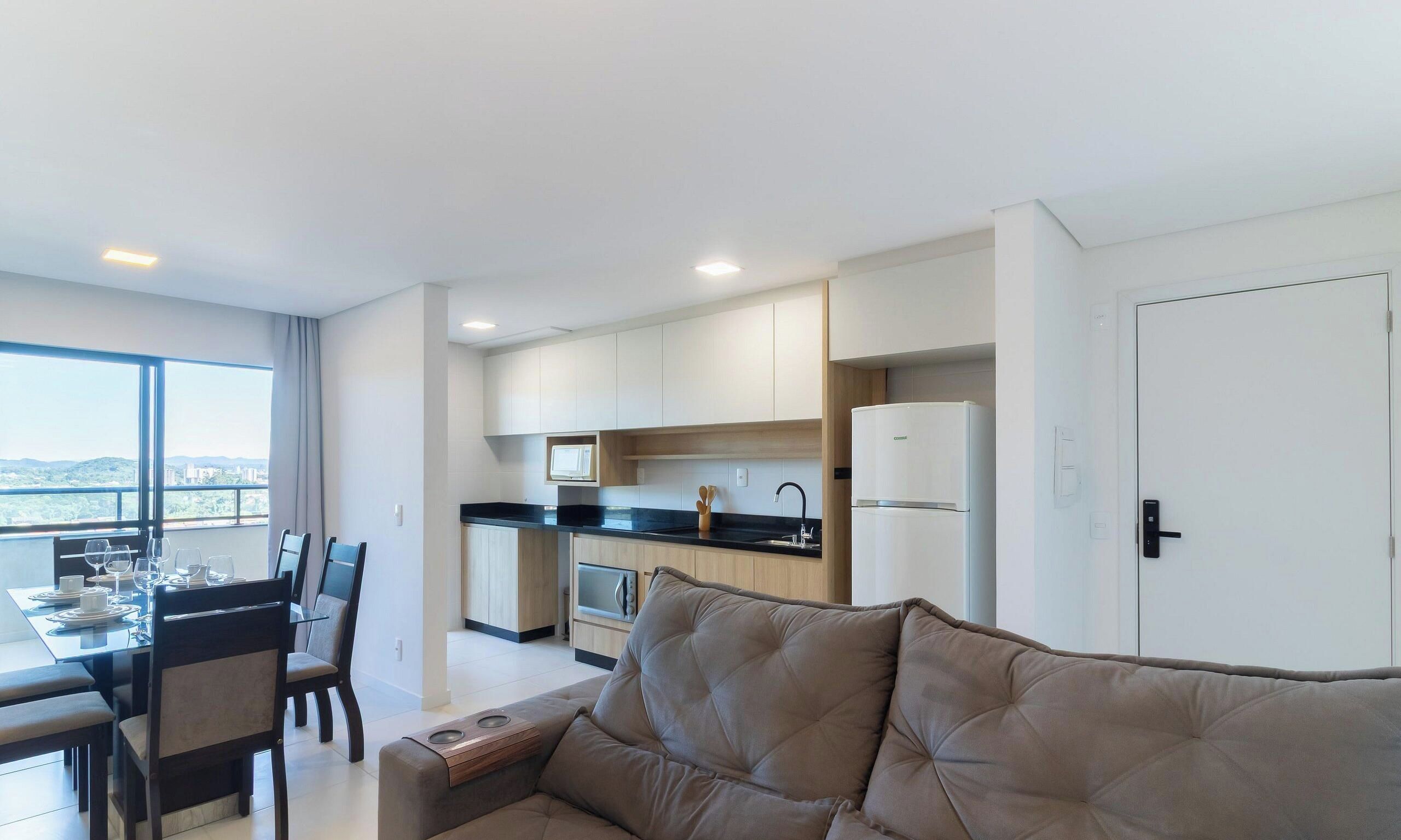 Una sala moderna con sofá, comedor con sillas y una mesa, y cocina con armarios y electrodomésticos.