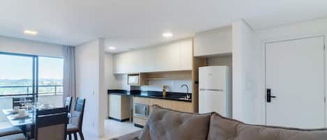 Una sala moderna con sofá, comedor con sillas y una mesa, y cocina con armarios y electrodomésticos.