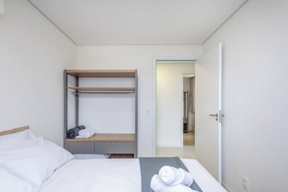 Une chambre d’hôtel avec un lit, une étagère en bois et une porte donnant accès à la salle de bain.