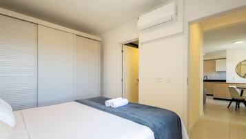 A hotel room with a bed, a wardrobe, an air conditioning unit, and a view into the kitchen area.